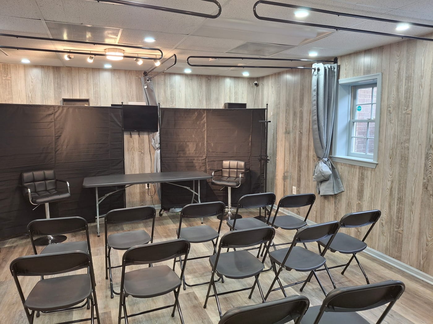Classroom seating in the back salon facing a presenter's table, two bar stools, and a wall-mounted screen