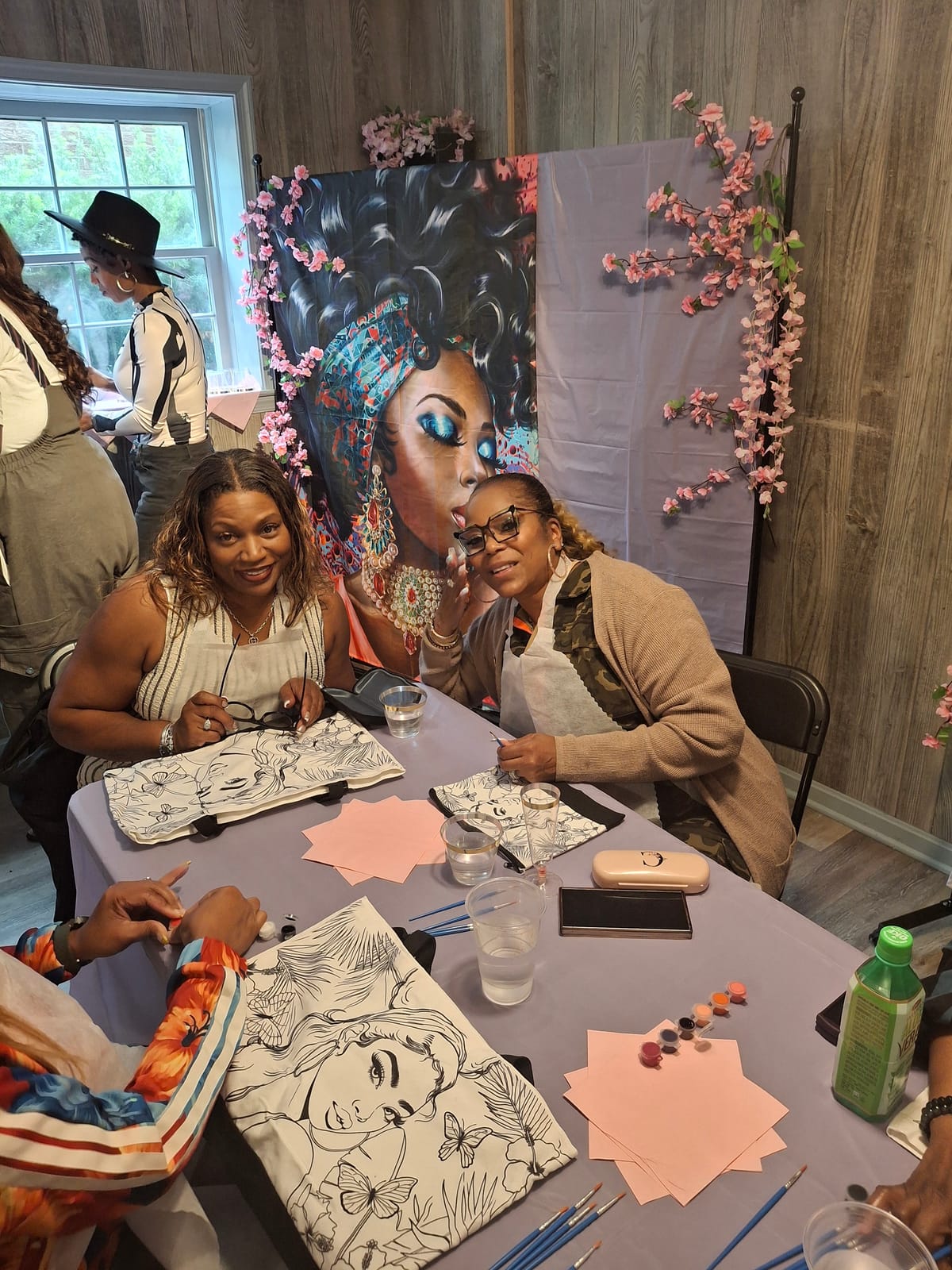 Two guests smiling over their tote bags in front of the floral backdrop
