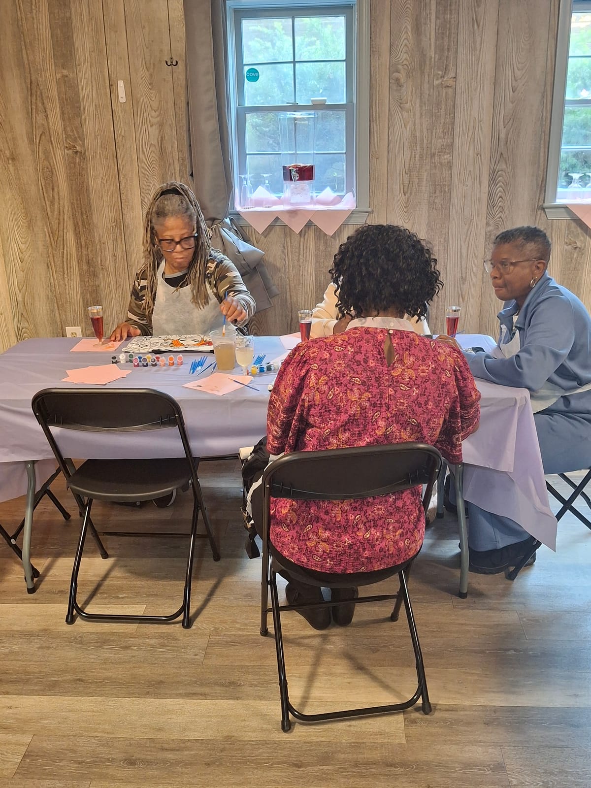 Three guests working on their designs at a table during the sip and paint
