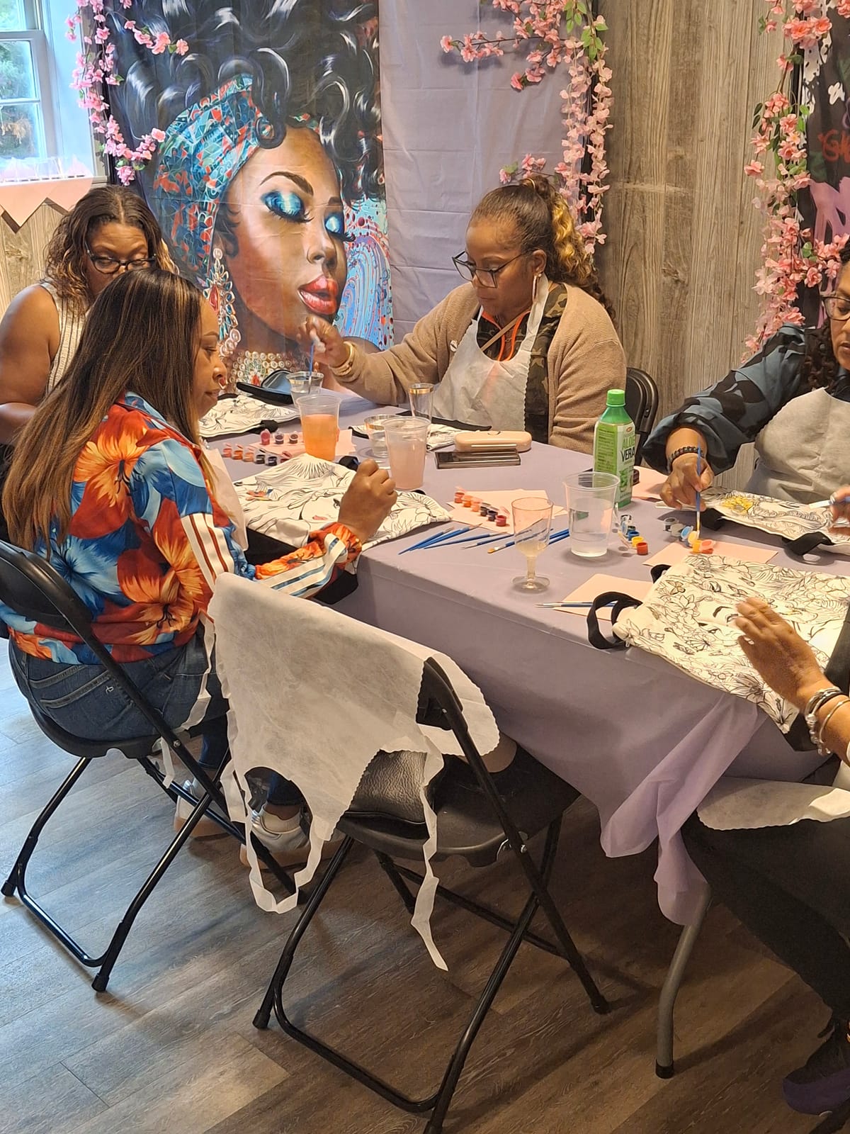 Guests painting pre-drawn tote bags around a table set with paints, brushes and drinks